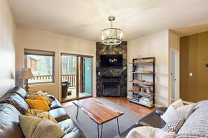 A living room with a fireplace, a sofa, a coffee table, and a bookshelf. - Hanging Glacier Chalet - Group Lodge - Sauna (Girdwood)