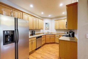 A kitchen with wooden cabinets, a stainless steel refrigerator, a dishwasher, and a coffee maker. - Hanging Glacier Chalet - Group Lodge - Sauna (Girdwood)