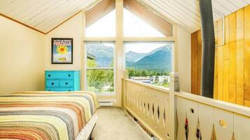 Un dormitorio con cama, cómoda, ventana grande con vistas a la montaña y chimenea.
