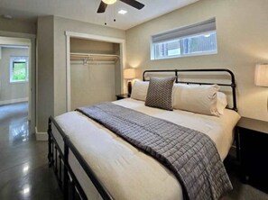 Une chambre à coucher comprenant un lit, des tables de chevet, un ventilateur de plafond, une fenêtre et un dressing.