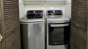 A laundry room with two stainless steel appliances, a dryer, and a washing machine. - The Monarch Lower Level | Updated 3BR Suite| Patio (Girdwood)