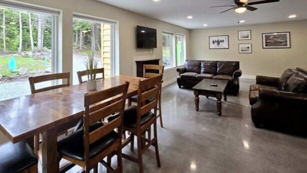 A spacious living room with a wooden dining table, leather couches, and a ceiling fan. - The Monarch Lower Level | Updated 3BR Suite| Patio (Girdwood)