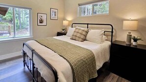 A bedroom with a bed, bedside tables, a window, and a view of the outdoors. - The Monarch Lower Level | Updated 3BR Suite| Patio (Girdwood)