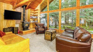 A wooden interior with a fireplace, leather furniture, and large windows overlooking a forest.