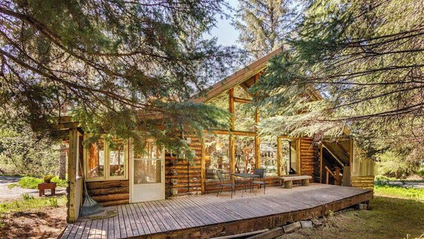 A wooden cabin with a deck, large windows, and a staircase leading to an upper level.