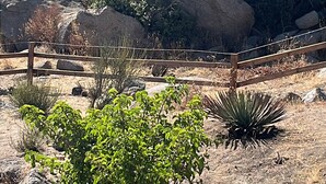 Paisatge rocos amb grans roques, una tanca de fusta i vegetació escassa.