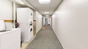 Ein Hotelkorridor mit einer Wäscheraum-Ecke links, einem Teppichboden und einer schlichten Wand.