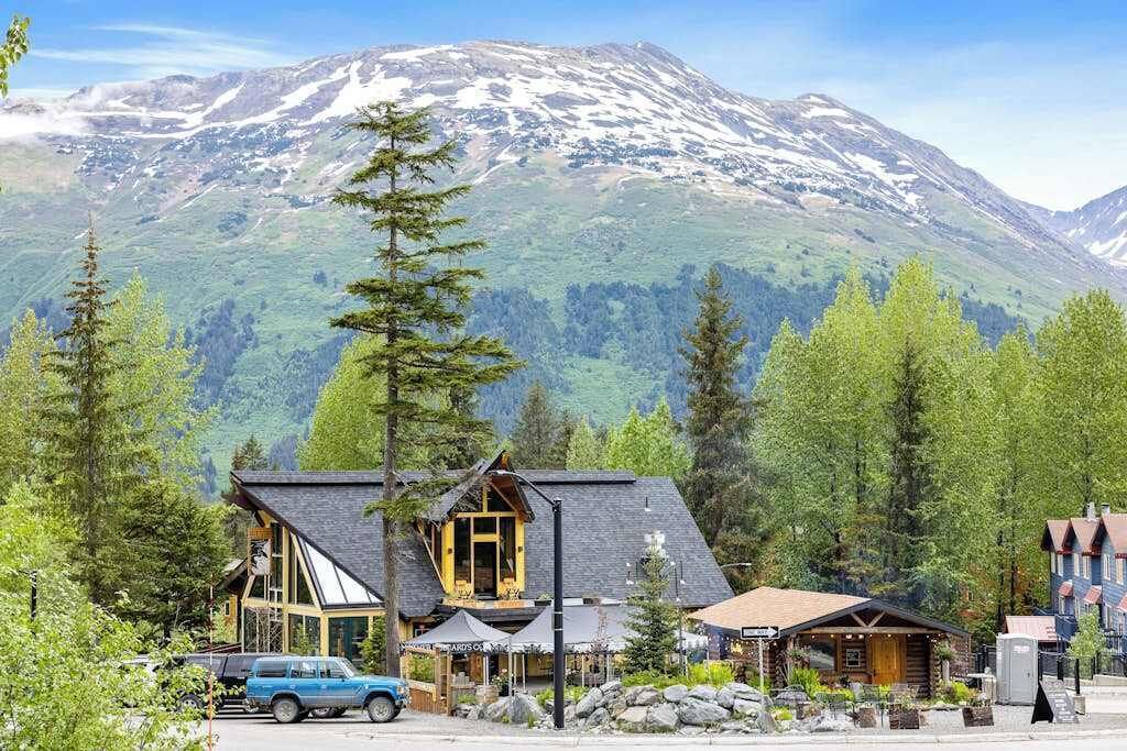 A lodge with a mountain backdrop, featuring a prominent building with a sloped roof and a smaller structure with a gabled roof.