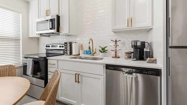 A modern kitchen with white cabinetry, stainless steel appliances, and a dining area with wicker chairs. - Iberville Inn•2 Kings•Family Friendly•FastWiFi (Lafayette)