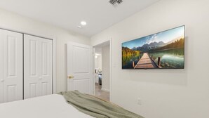 A bedroom with a bed, a painting of a lake and mountains, and a door leading to a bathroom. - Iberville Inn•2 Kings•Family Friendly•FastWiFi (Lafayette)