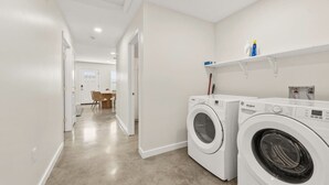 A laundry room with two front-loading washers, a dining area with chairs, and a hallway leading to another room. - Iberville Inn•2 Kings•Family Friendly•FastWiFi (Lafayette)