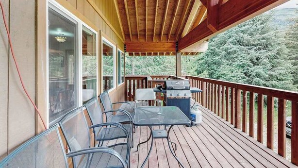 Una terraza techada con mobiliario exterior, una parrilla y vistas a una zona boscosa.