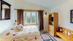 A bedroom with a bed, a ceiling fan, a wardrobe, a bench, and a window with curtains.