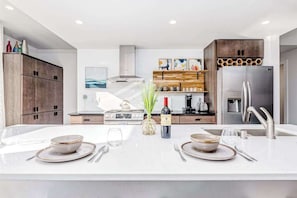 Une cuisine moderne dotée d’un îlot central, d’appareils électroménagers en acier inoxydable et de meubles de rangement en bois.