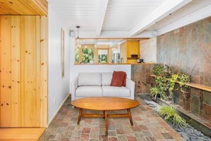 Ein modernes Interieur mit einer Steinsäule, einer hölzernen Bank, einer Couch und einer kleinen Pflanzengruppe.