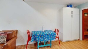 A room with a dining table, chairs, a sofa, and a white wardrobe. - Kabina on Vail | Lofted Cottage | Spiral Stairs (Girdwood)