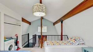 A bedroom with a bed, a washing machine, a radiator, and a staircase leading to an upper level. - Kabina on Vail | Lofted Cottage | Spiral Stairs (Girdwood)