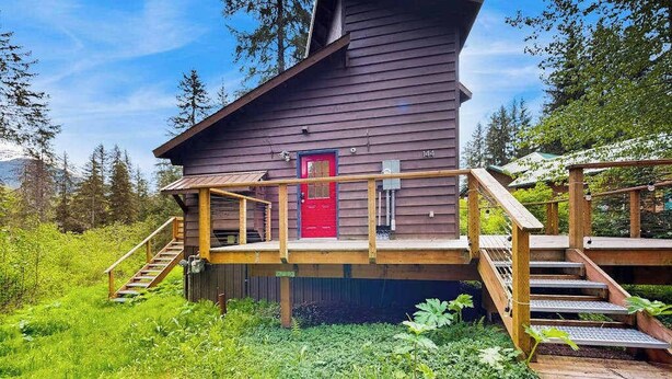 A wooden cabin with a red door, wooden stairs, and a deck.