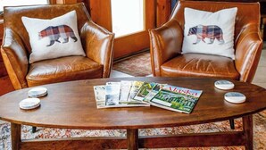 Zwei braune Ledersessel mit Bären-Kissen, ein Couchtisch mit Zeitschriften und ein Klavier im Hintergrund.