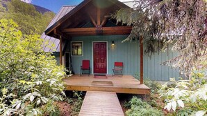 A cabin with a wooden deck, a red door, and two red chairs.