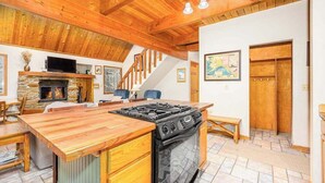 A kitchen with a wooden island, stove, and stone fireplace.