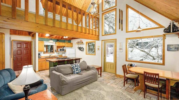 A spacious living area with a high ceiling, wooden beams, a dining table, and a sofa.
