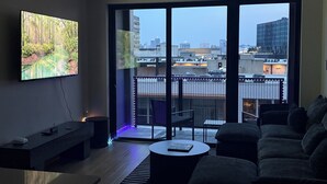 En moderne stue med et fladskærms-tv, en sofa, et sofabord og en balkon med udsigt over byen.
