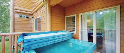 Eine Holzterrasse mit Whirlpool, einem überdachten Bereich und einer Glasschiebetür, die zu einer weiteren Terrasse führt.