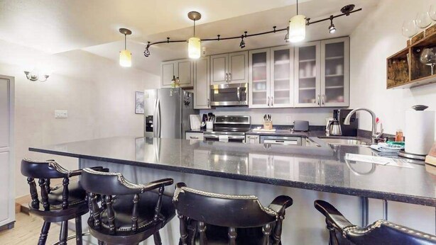 A kitchen with a central island, bar stools, stainless steel appliances, and pendant lighting. - North 409 | Ski-In/Out | Vintage Ski Decor (Anchorage)