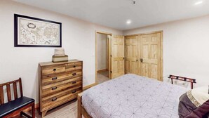A bedroom with a bed, wooden dresser, a chair, and a wardrobe. - North 409 | Ski-In/Out | Vintage Ski Decor (Anchorage)