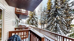 A wooden deck with snow-covered railings, a covered porch, and snow-laden trees in the background. - North 409 | Ski-In/Out | Vintage Ski Decor (Anchorage)
