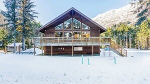 Uma cabana de madeira com varanda, rodeada por neve e árvores.
