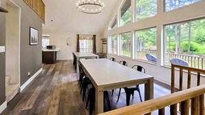 Um quarto espaçoso com uma mesa comprida, cadeiras, um candelabro, janelas amplas e vista para o verde lá fora.