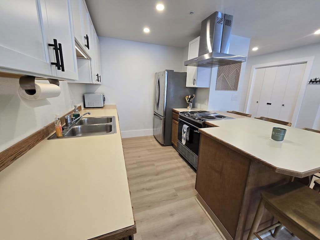 A modern kitchen with white cabinets, a stainless steel refrigerator, and a wooden countertop.