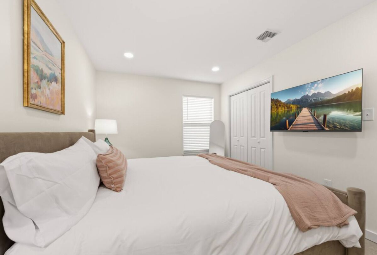 A bedroom with a bed, a painting, a door, and a window.