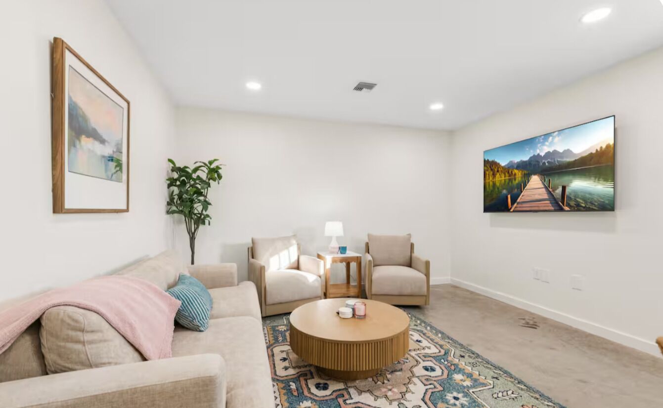 A living room with a sofa, two armchairs, a coffee table, a rug, and two paintings on the walls.