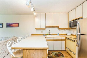 A compact kitchen with white cabinets, a central island, a microwave, and a refrigerator.