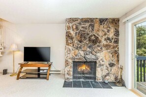 A living room with a stone fireplace, a flat-screen TV, and a wooden coffee table.