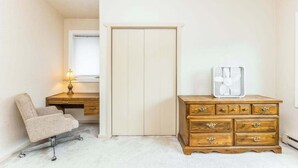 Een slaapkamer met een bureau, een stoel, een kledingkast en een ventilator.
