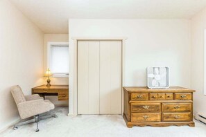 A bedroom with a desk, a chair, a wardrobe, and a fan.