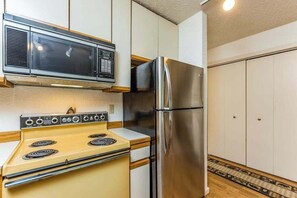 A kitchen with a yellow stove, stainless steel refrigerator, and a microwave above the stove.
