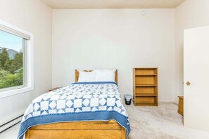 A bedroom with a bed, a window, a bookshelf, and a door.