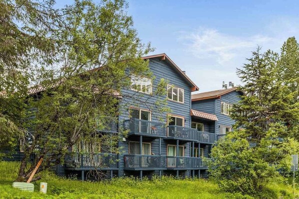 A multi-story building with balconies, surrounded by greenery.