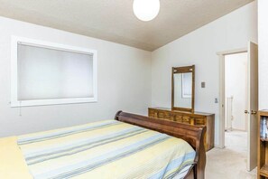 Ein Schlafzimmer mit einem Bett, einer Kommode, einem Spiegel und einem Fenster mit Jalousien.