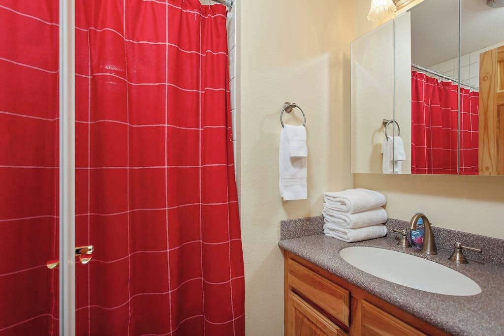 A bathroom with a red shower curtain, a sink with a mirror, and stacked white towels.