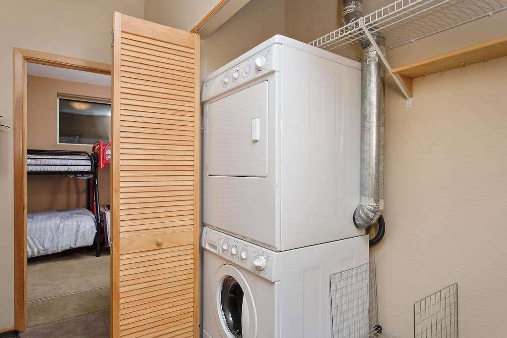 A laundry room with stacked washers and dryers, a wooden door, and a window in the background.