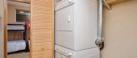A laundry room with stacked washers and dryers, a wooden door, and a window in the background.