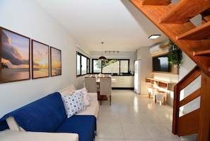 A modern living room with a sofa, dining area, kitchen, and staircase.