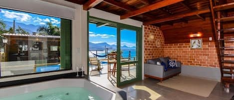 A room with a large window, a jacuzzi, a sofa, and a view of the sea.