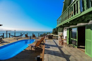 Eine Holzterrasse mit Pool, Sitzgelegenheiten im Freien und Blick auf das Meer.